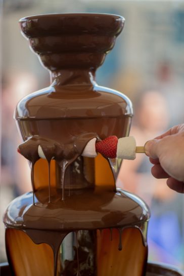 Fontanna czekolady i dłoń trzymająca szaszłyka z pianek i truskawek