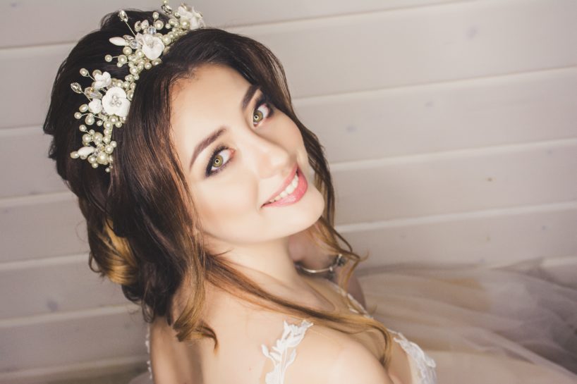 Uśmiechnięta Panna Młoda prezentująca ślubny makijaż i fryzurę z ozdobną opaską z pereł