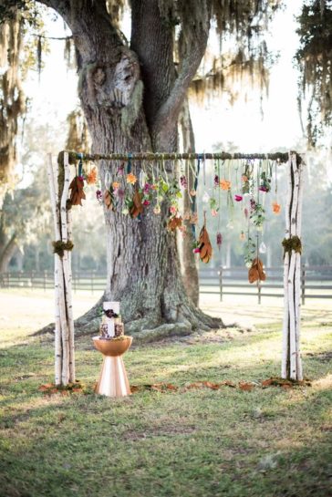 Drewniana dekoracja ślubna z zawieszonymi na niej jesiennymi liśćmi, w tle duży, tort ślubny