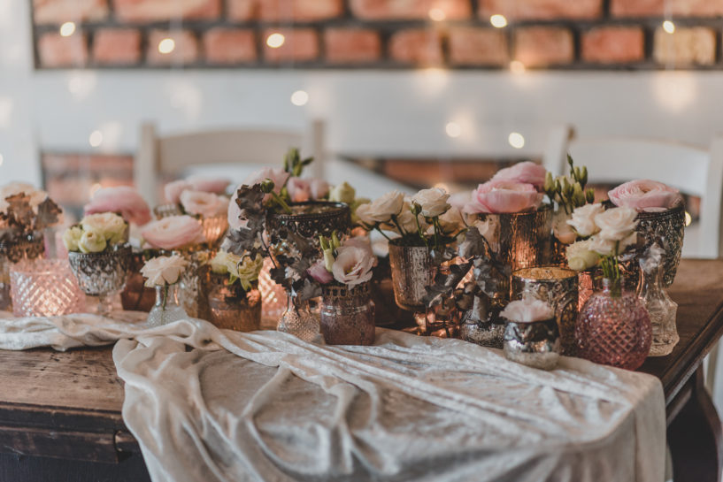 Szereg wazonów i świeczników wypełnionych świecami i kwiatami ułożonymi na drewnianym, dużym stole